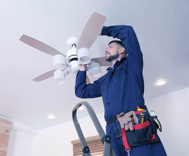 Electrician Installing Ceiling Fan With Lamps Indoors