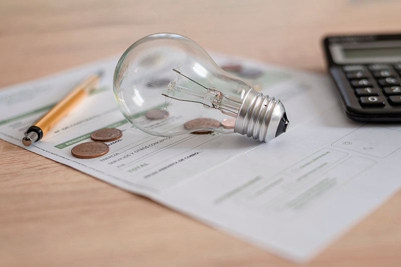 Electricity bill on a table with coins, a calculator, a pen, and a light bulb.