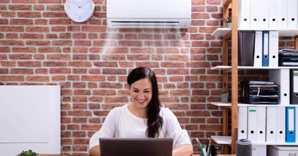Woman working on a laptop at a wood desk while being cooled by an efficient air conditioner.