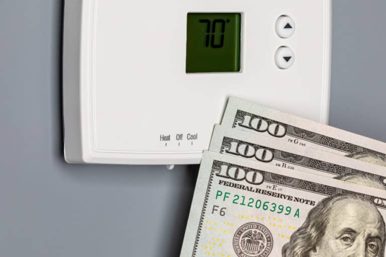 Hundred dollar bills in front of a thermostat.
