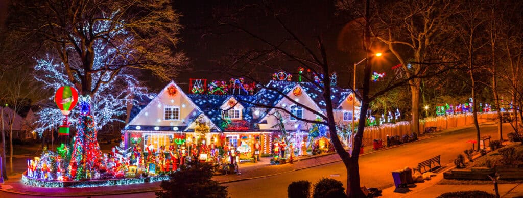 Suburban street at night with houses covered in Christmas lights.