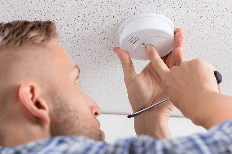 person testing a smoke detector while also holding a screwdriver
